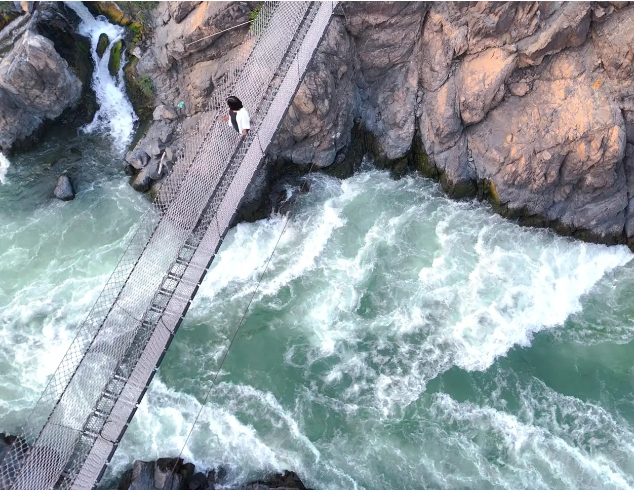 Rushing river rapids at Li Phi waterfall with a suspension viewpoint bridge
