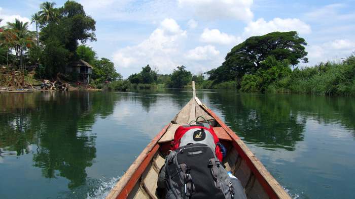 A traditional longtail boat navigating past lush green islands inside the 4000 islands archipelago