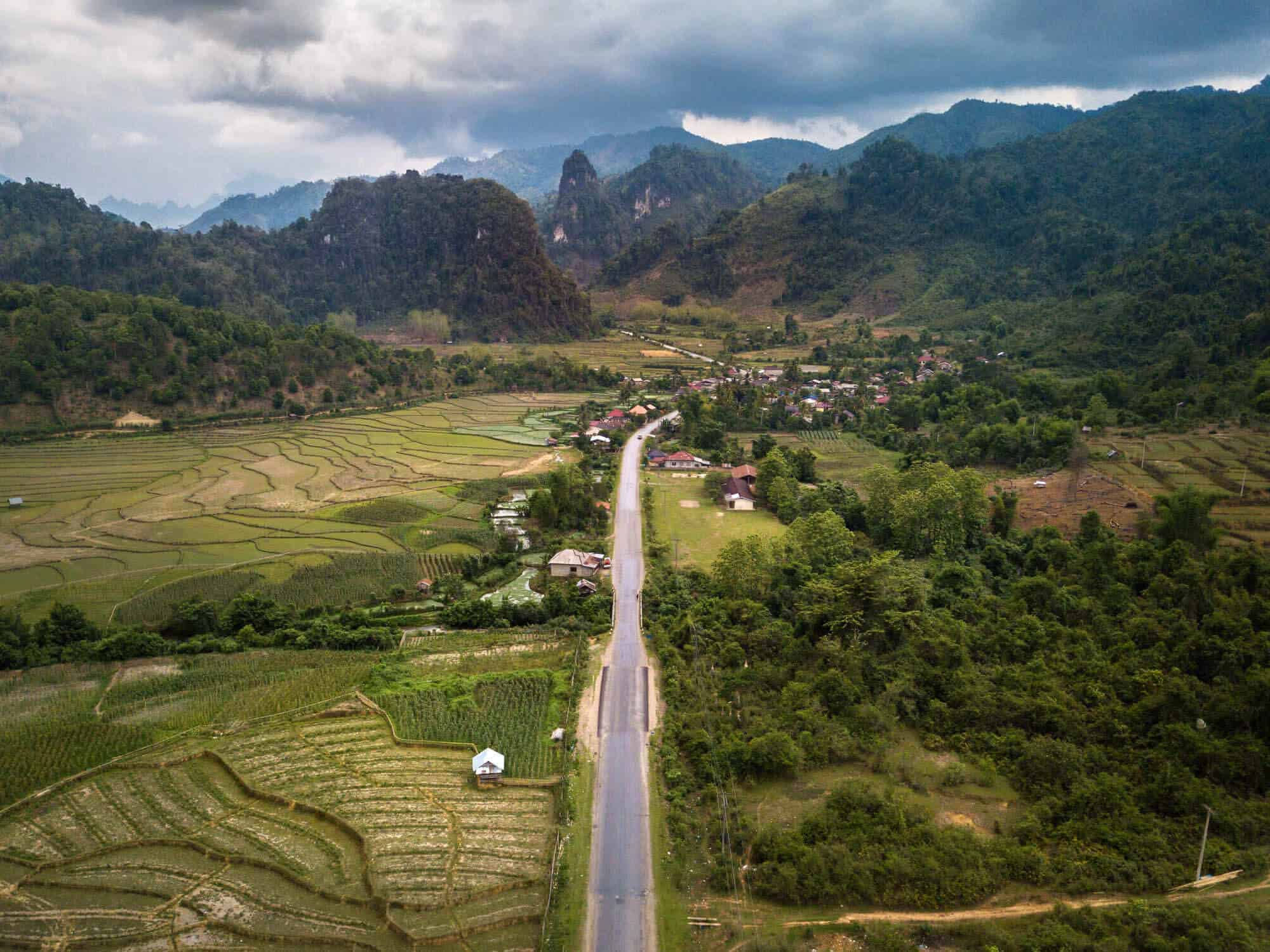 A rural highway stretching past green rice paddies and distant hills in southern Laos