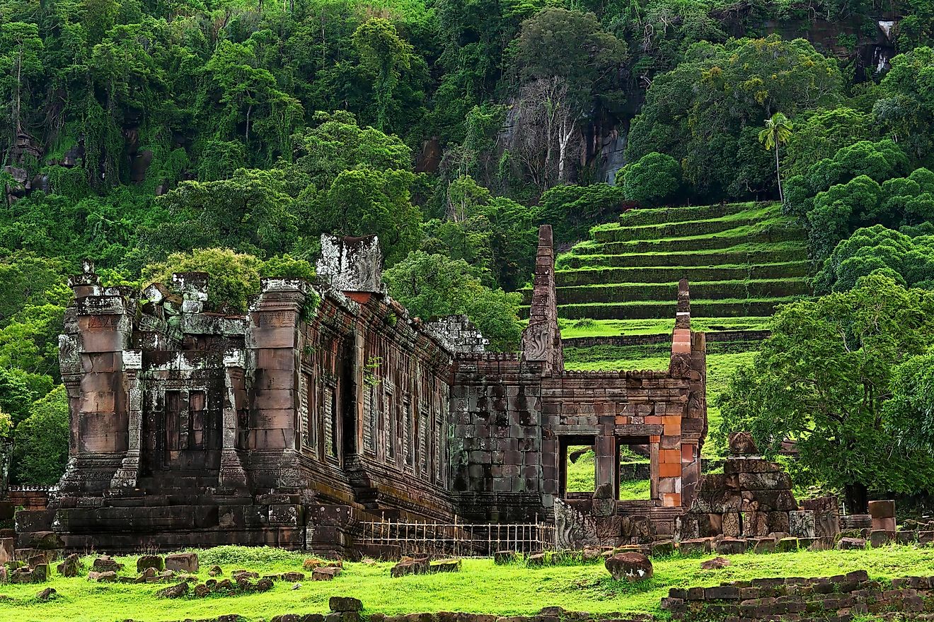 Ancient stone ruins and steep rock steps of Wat Phu temple under a large mountain cliff